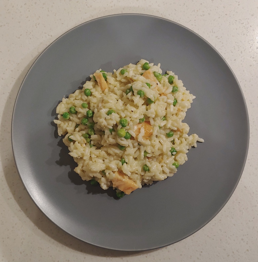 Smoked salmon risotto with visible peas and pieces of salmon sitting on a grey plate.