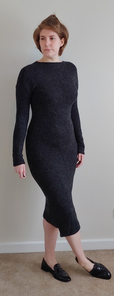 Full length photo of Helen wearing a dark grey knitted dress, with long sleeves and an uneven hem.