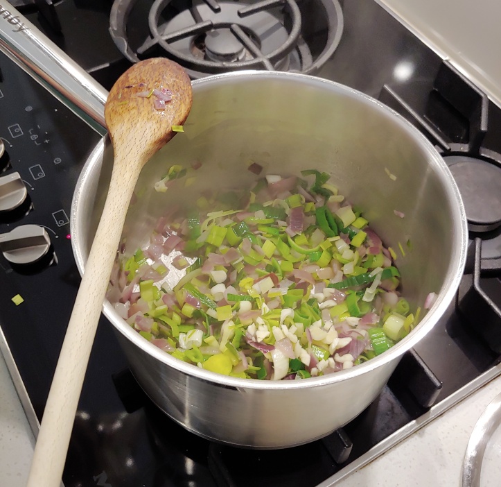 Leek and red onion sweating in a stainless steel pan.